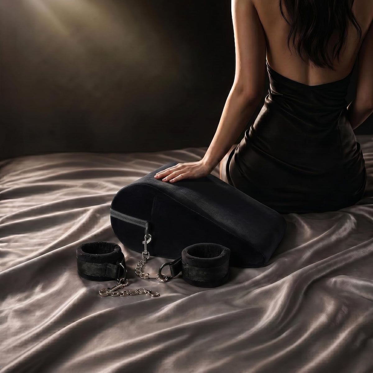 Black plush positioning pillow with two cuffs and chain hardware on a bed