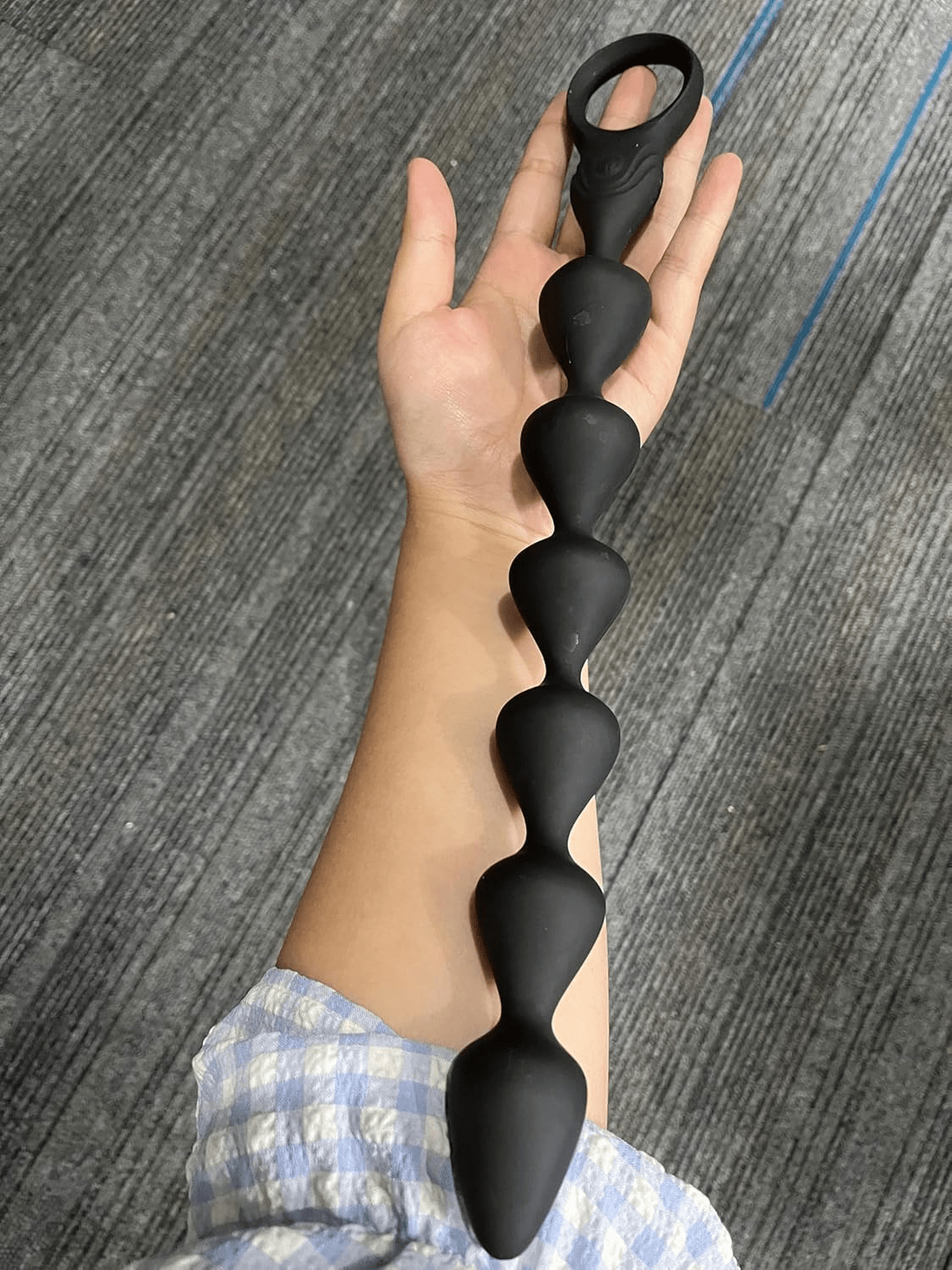 Black segmented vibrating anal beads held in one hand, with flared base and loop handle.